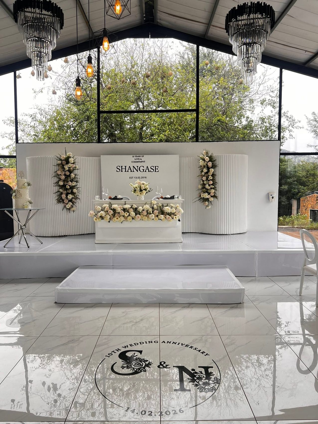Fluted white stage backdrop with floral columns, a tiered cake and a monogrammed dance floor